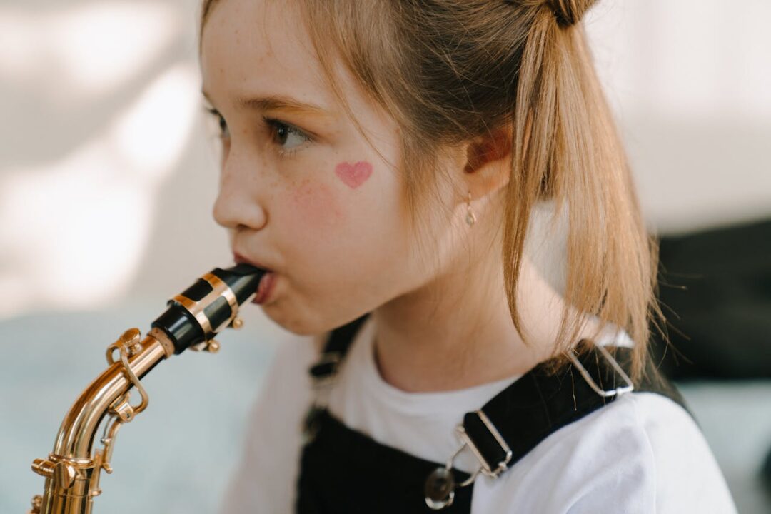 pexels-photo-4709820 A young girl with heart face paint plays the saxophone indoors, exuding youthful creativity.