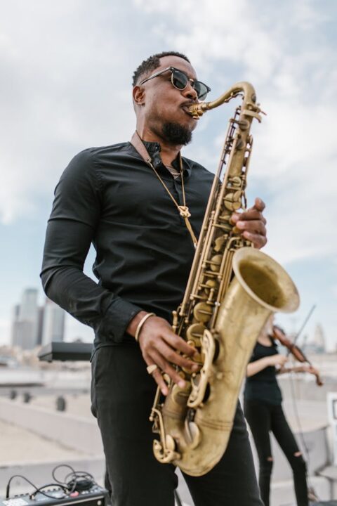 pexels-photo-7503368 A talented musician playing saxophone under a clear sky with urban skyline in the background.