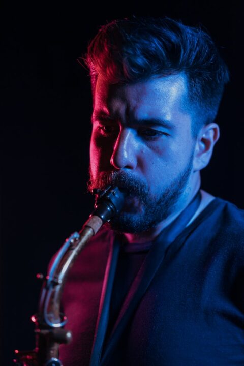 pexels-photo-7586588 Close-up of a bearded musician playing saxophone under dramatic studio lighting.