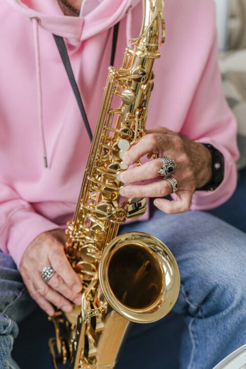 pexels-photo-8929058 A saxophonist wearing rings and a pink sweater plays music in a casual setting.